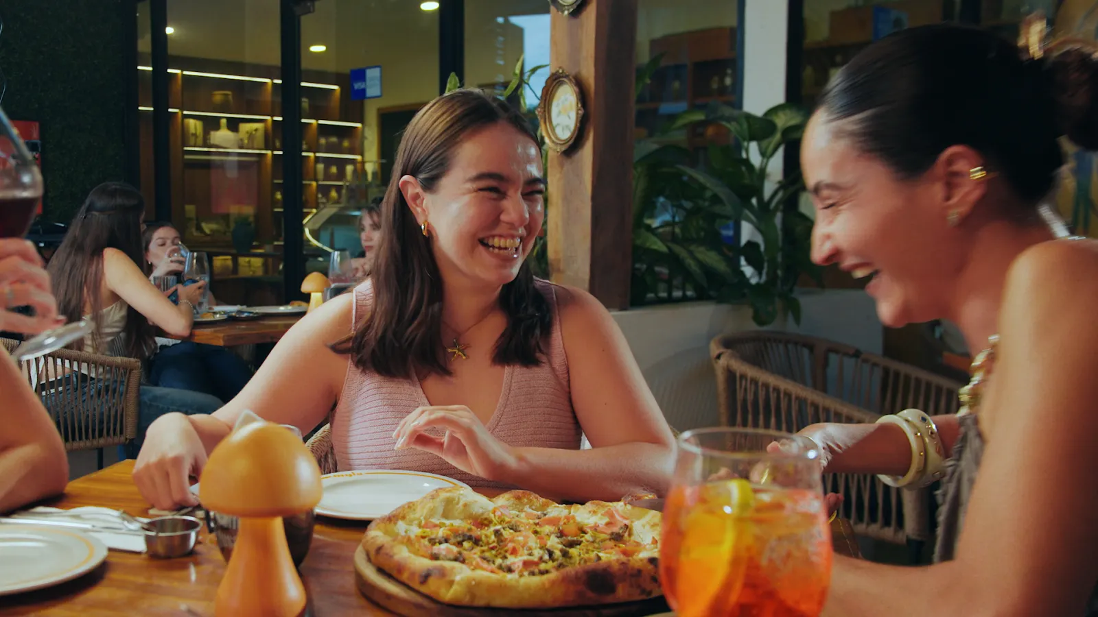 Amigas compartiendo pizza de masa madre y Aperol en Mylo Cancún